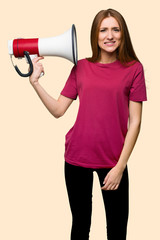 Young redhead girl taking a megaphone that makes a lot of noise on isolated yellow background