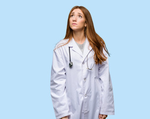 Redhead doctor woman looking up with serious face on isolated blue background