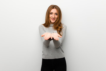 Redhead girl over white wall holding copyspace imaginary on the palm to insert an ad