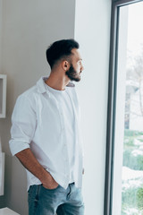 Pensive man standing with hand in pocket and looking at window