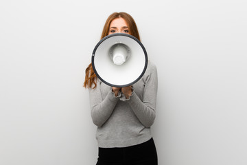 Redhead girl over white wall shouting through a megaphone to announce something
