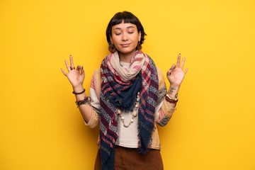 Young hippie woman over yellow wall in zen pose