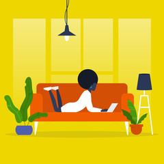 Fototapeta premium Young black female manager lying on a sofa with a laptop