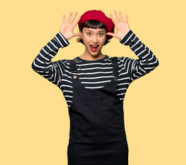 Fototapeta premium Young woman with beret with surprise and shocked facial expression over yellow background