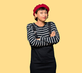 Young woman with beret making doubts gesture while lifting the shoulders over yellow background