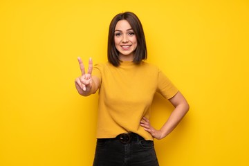 Young woman over yellow wall smiling and showing victory sign