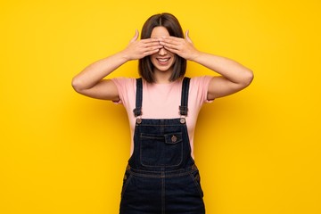 Young woman over yellow wall covering eyes by hands. Surprised to see what is ahead