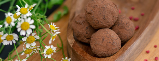 Round chocolates on a wooden plate next to the summer beautiful delicate chamomile flowers.banner.