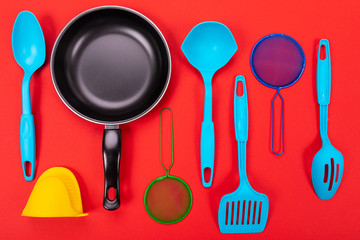 Frying pan with kitchen utensils isolated on red background