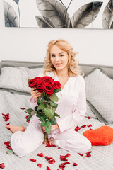 Pretty woman in pajama sitting on bed with roses