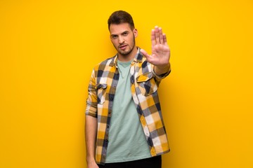 Handsome man over yellow wall making stop gesture denying a situation that thinks wrong