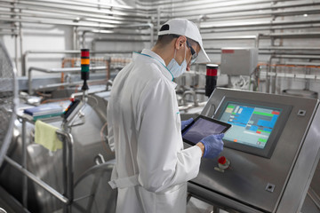Technologist stands with a tablet near the digital screen at the dairy Plant