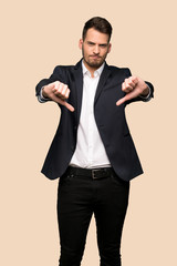 Handsome business man showing thumb dowg with negative expression over ocher background