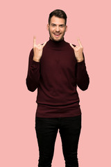 Man with turtleneck sweater making rock gesture over pink background