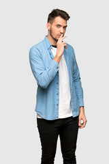 Handsome man showing a sign of silence gesture putting finger in mouth over grey background