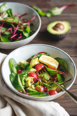 Vegetarian healthy salad is made from swiss chard leaves, cherry tomatoes, avocado, lemon juice and olive oil into a ceramic portion bowl.