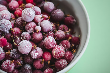 A mixture of red frozen berries of currant and gooseberry covered with white frost in a white plate on the table.