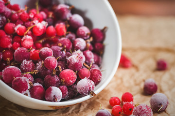 Red frozen berries of currant and gooseberry, covered with white frost, in a white plate and on the table. Healthy eating concept