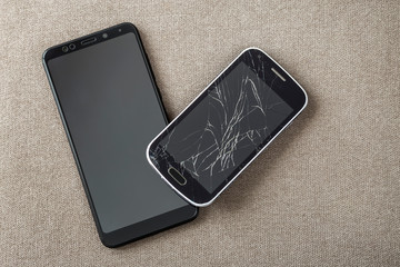 Comparison of two black mobile phones, old cellphone with cracked screen and new modern on light...