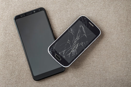 Comparison of two black mobile phones, old cellphone with cracked screen and new modern on light cloth copy space background. Technology progress and replacement concept.