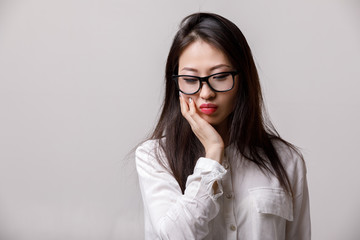 portrait of sad asian woman in glasses and white shirt on gray background. emotions