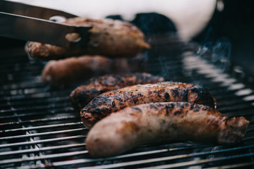 selective focus of grilled tasty meat sausages and tweezers on barbecue grid