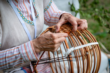 Old woman in national costume make local wicker basket. Traditional handicrafts concept. Latvia - Image