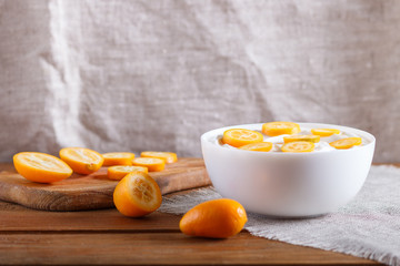 greek yogurt with kumquat pieces in a white plate on a brown wooden background