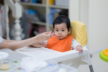feeding 9 months asian baby girl on high chair. mom feeds blend food to her daughter.Traditional Weaning