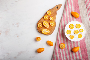 greek yogurt with kumquat pieces in a white plate on a white wooden background