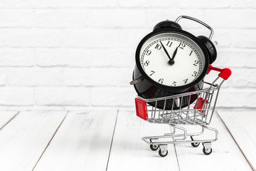 Alarm clock in trolley shopping cart on white wood background with copy space. time concept.