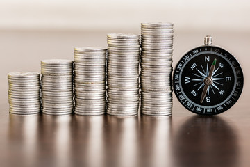 Stack of coins with compass on wood table