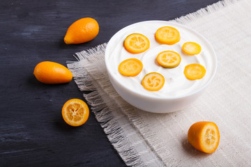 greek yogurt with kumquat pieces in a white plate on a black wooden background