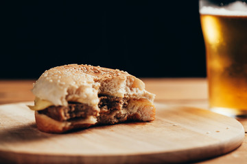 Bitten cheeseburger and beer glass on wooden table