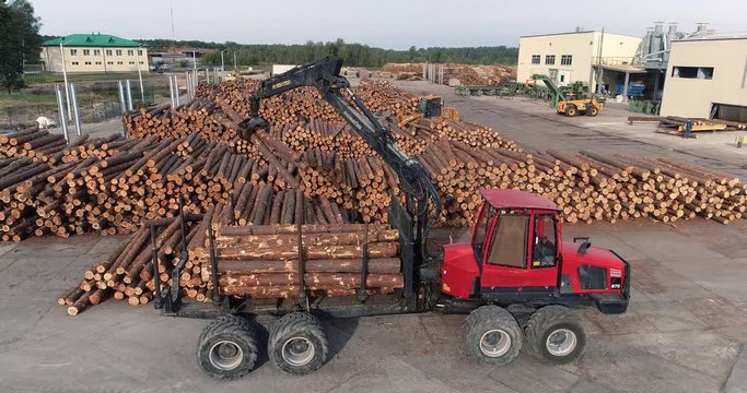 A forwarder transports the logs at the Sawmill Factory. A forestry forwarder uses a log grapple to load logs. A pile of logs on a Log yard. Sawmill Industry. Aerial View.	