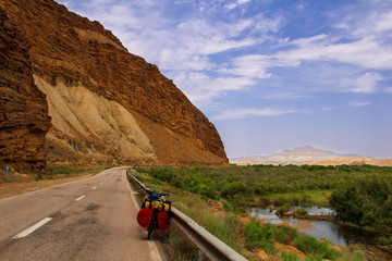 Fototapeta premium IranBike to travel in the road of Iran with a valley and green grass on the side. Orange rocks and desert mountains