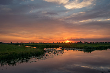 Fototapeta na wymiar The sun sets on the horizon of the dutch countryside. A beautiful colored sky is reflected in the water of a lake. 