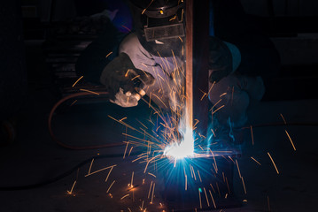 Welding skills training of welder with protective mask and welding steel metal part.