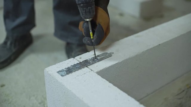 builder screwing joining clamp in aerated concrete block with electric drill