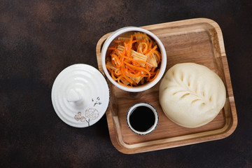 Wooden serving tray with korean steamed traditional tin-pun, salad and dipping sauce. Flatlay on a brown metal background