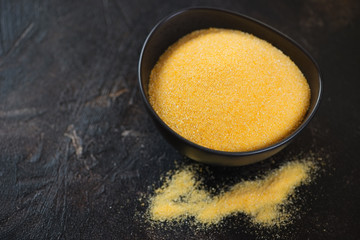 Bowl of raw polenta on a dark brown stone background, horizontal shot with copyspace