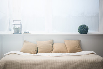 bedroom with brown pillows and white blanket on empty bed, plants and glasses