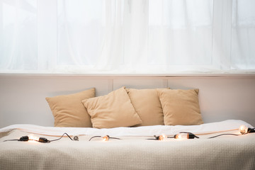 empty bed with brown pillows, white blanket and festoon lights