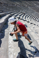 Young tourist boy in the hat with camera runs up on the Ancient Theatre of Epidaurus, Peloponnese, Greece