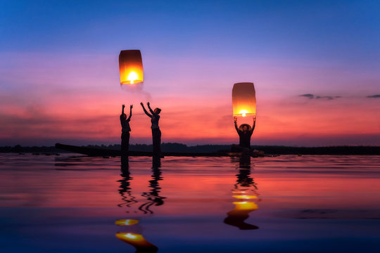 Multi-generation family flying sky lanterns on Mekong river at sunset, Thailand