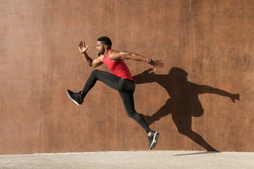 Young black man running and jumping casting shadow on a wall.