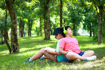 Two Asian boys sitting reading books and listening to music in the garden