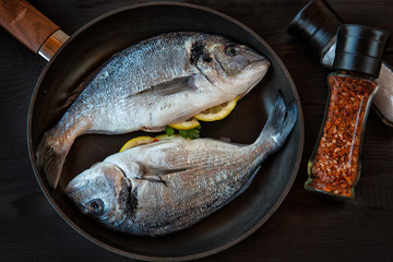 Fresh Dorado fish, with vegetables, herbs, lemon in a frying pan.