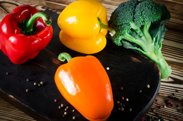 Juicy red and orange peppers with with a green tail lies next to Bundle of broccoli are on a brown...