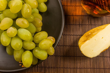 large brush of green grapes in a ceramic plate, a decanter and a glass of wine and cheese